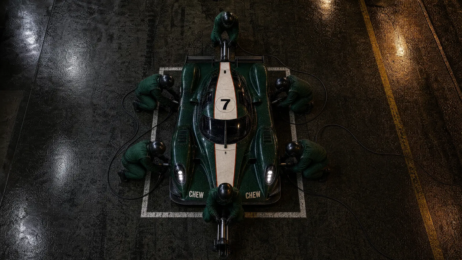 Overhead view of the green race car stopped in its pit box at night, six crew working around it at once.